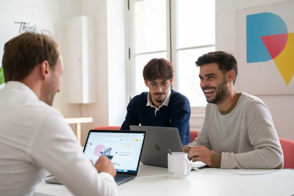 Équipe d'hommes souriants en pleine discussion devant leurs ordinateurs, collaborant sur des projets d'UX et UI design sur mesure, avec une approche centrée sur l'humain et l'éco-conception.